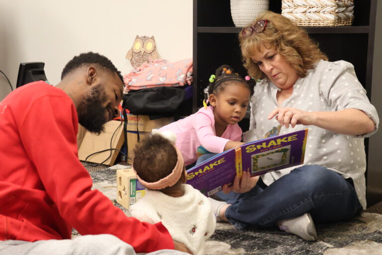 Two young children sit on the floor with two adults for story time